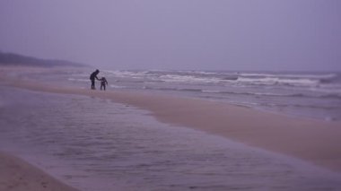 Mother and daughter walking on sea coast in cold weather