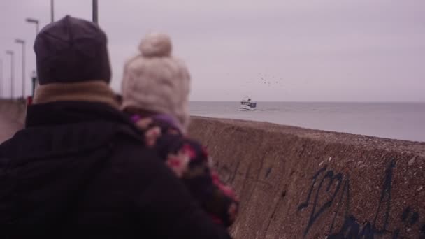 Femme tient une fille sur les mains et regarde vers un navire plus proche — Video