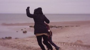 Mother and daughter spending time on sea coast in cold weather