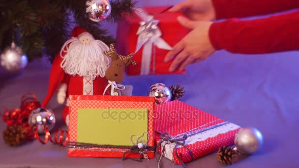 Una gran cantidad de juguetes de Navidad se ponen bajo el árbol de abeto por manos femeninas, incluyendo Santa Claus, caja roja y marco de fotos de Navidad — Vídeos de Stock