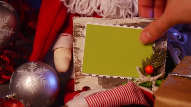 Las manos masculinas toman el marco hecho a mano de la foto debajo de un árbol decorado del abeto de Navidad, con un montón de bolas chispeantes que mienten en un piso violeta — Vídeo de stock