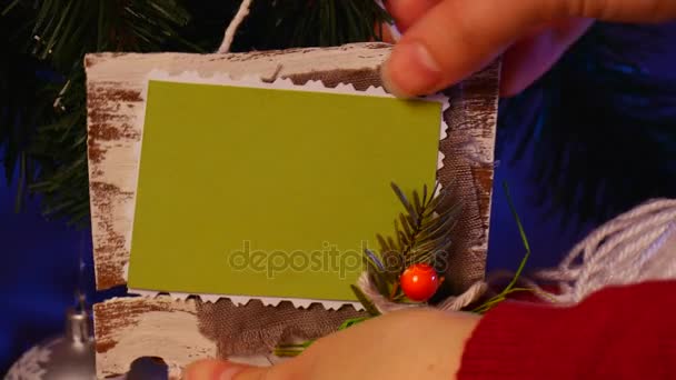 Las manos del hombre cuelgan un bolsillo hecho a mano con un marco de fotos en una rama de un árbol de Navidad, decorado con brillantes bolas blancas — Vídeos de Stock