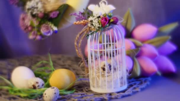 Codorniz de Páscoa e ovos de galinha em uma mesa e em um anel amarelo pendurado com um monte de flores rosadas deitado nas proximidades — Vídeo de Stock