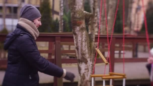 Anne kızı bir çocuk Swing binmek için yardımcı olur — Stok video