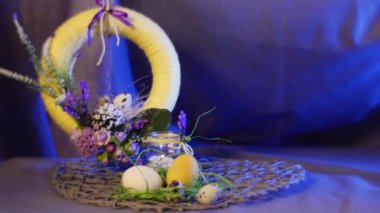 Opole, Poland - Feb 18 2017: Beautiful Yellow Fabulous Field Flowers on an Easter Ring, Hanging Over Traditional Hen and Quail Eggs on a Round Table, With a Violet Background Behind It, Being Shot With a Steadicam Camera