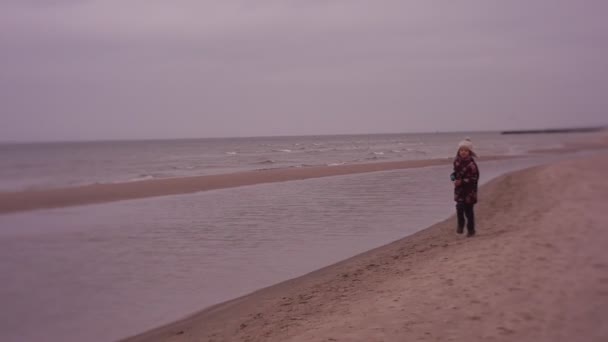 Boldog gyermek fut mentén a tenger és a hívások anya, a lány fut, hogy az anyja, a tenger partján, télen — Stock videók
