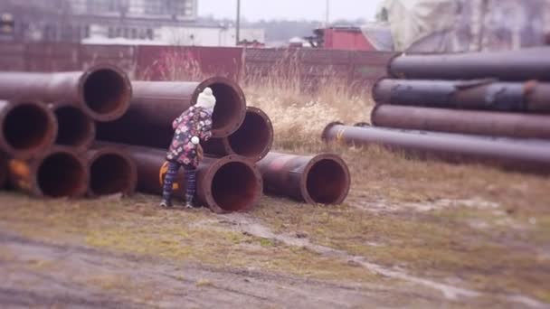 Uma menina, uma criança em um canteiro de obras olha em um tubo de grande diâmetro, jogos perigosos em um edifício abandonado, construção abandonada — Vídeo de Stock