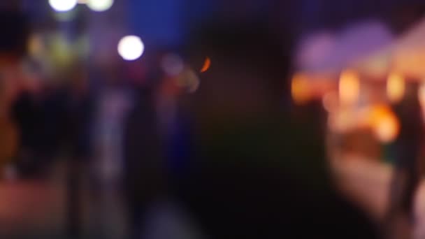 Rušnou ulici ve městě večer s auto světla a temné siluety lidí rozostřené pozadí zářivě barevné osvětlení. Z Focus, rozmazané — Stock video