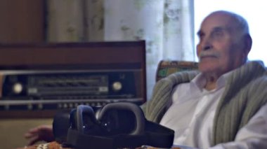 Kafkasyalı kıdemli adam evdeki retro radyosunda müzik dinliyor.