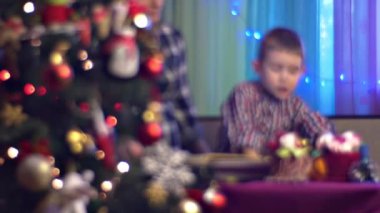 Anne ve oğlu evde Noel ağacının yanında kitap okuyor.