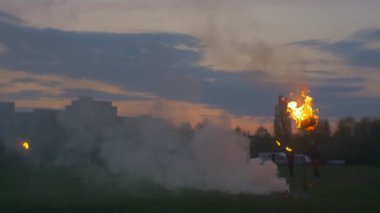 Ateş yakan adamlar, alacakaranlıkta siluetler. Erkekler koşuyor, Ateşin etrafında yürüyor, Duman yükseliyor. Ağır çekim. Büyük Yanan Meşaleler. Ulusal Tatil, Şehrin Sınırında Gösteriler