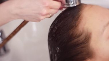 Saç istemci bir güzellik salonu durulama, kadın Kuaför Saç ile su, sulama olabilir bir elinde tutan bir kızın nemlendirir. Diğer elimle yavaşça yıkama köpük kozmetik kapalı. Yakın çekim