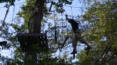 Turist Halat Yolu 'ndan Yürüyor, Siluet, Park' taki Adam, Yavaş Hareket. Turist ahşap kütüklerden adımlar atıyor, halatlara asılı, üsse ulaşmaya çalışıyor.