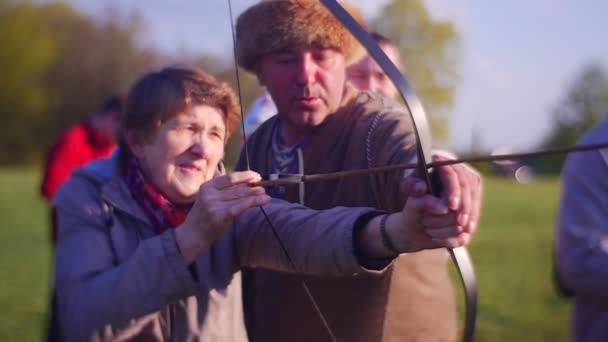 Hombre ayuda a anciana mujer a aprender cómo disparar flechas — Vídeos de Stock