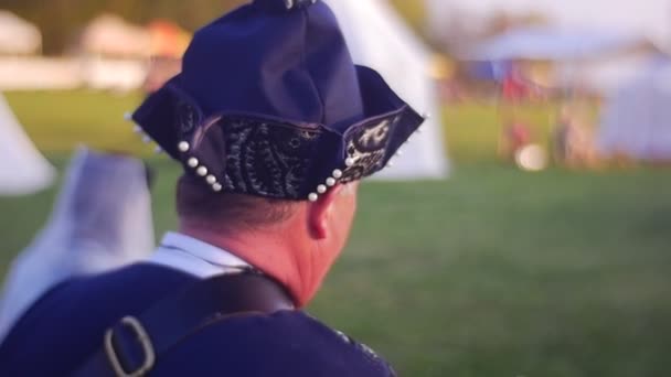 Man, gekleed in Caftan en wees van zwarte hoed, wandelingen langs een groen veld — Stockvideo