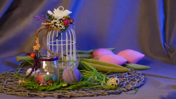 Marco de fotos festivo está siendo colgado en una jaula de huevo superior con un arco blanco, huevos de gallina y codorniz, una botella con una vela y tulipanes rosados cerca — Vídeos de Stock
