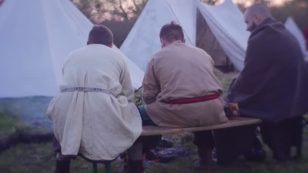 Ridder toernooi in Opole mannen zitten op een bankje in de buurt van een brand en praten historische re-enactment van een kamp van middeleeuwse Warriors witte tenten zijn lopen — Stockvideo