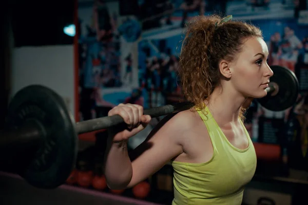 Chica joven haciendo sentadilla en el gimnasio con barra . — Foto de Stock