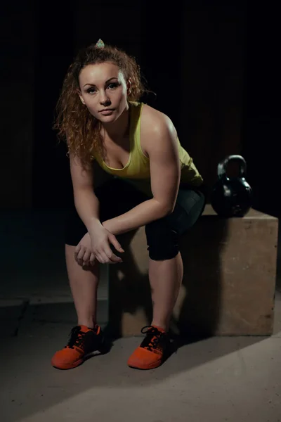 Mujer joven se sienta en un pedestal con pesas en el gimnasio — Foto de Stock