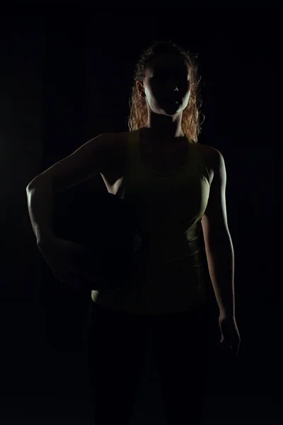 Jeune femme se tient avec la balle contre-jour et l'ombre dans la salle de gym — Photo