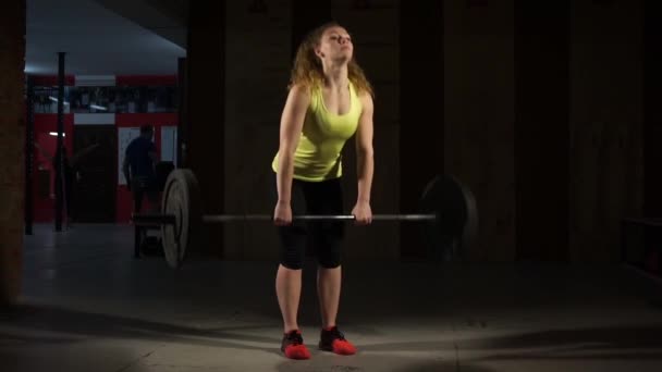 Mujer joven haciendo montacargas con una barra en el gimnasio . — Vídeos de Stock