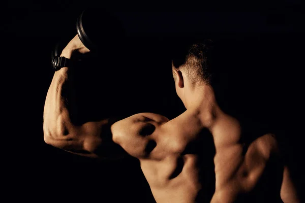 Bodybuilder mit Kurzhanteln auf dunklem Hintergrund. — Stockfoto