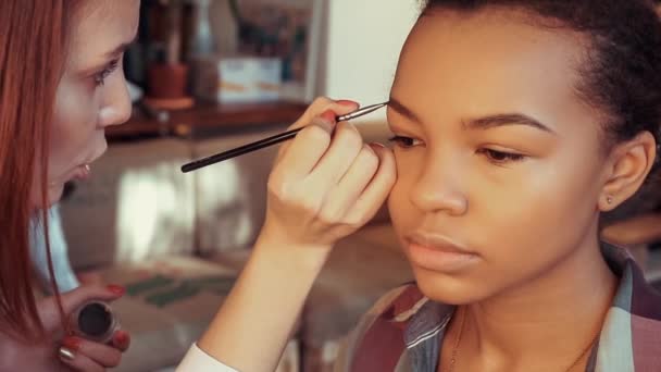 Maquillaje artista pinta las cejas de una joven hermosa modelo africana . — Vídeo de stock