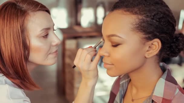 Maquillaje artista pinta el párpado de un joven modelo africano . — Vídeo de stock