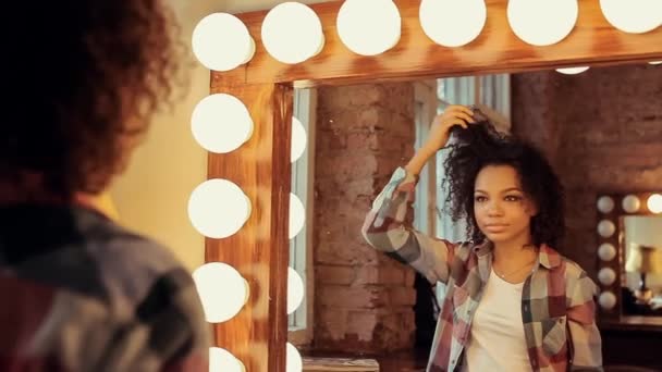 Schönes afrikanisches Model, das ihre Haare vor einem Spiegel berührt. — Stockvideo