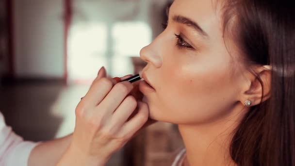 Make-up-Artist bemalt ihre Lippen eine schöne junge Brünette. — Stockvideo