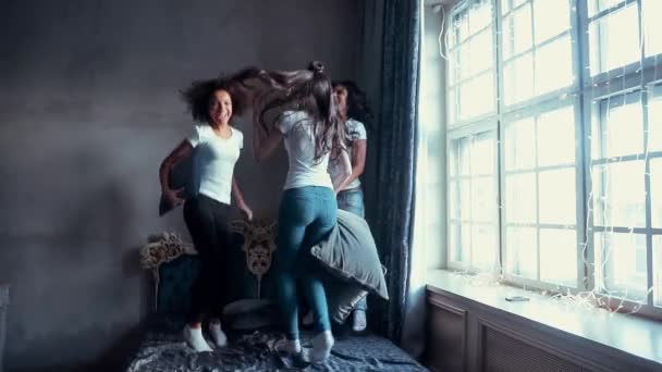 Tres chicas en camisas blancas saltan en la cama con almohadas en la mano . — Vídeo de stock