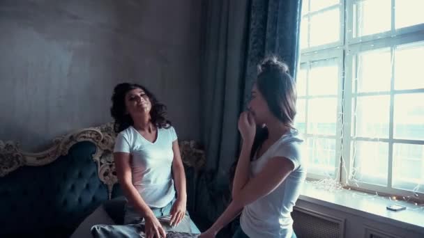 Twee meisjes in witte shirts op het bed met kussens in de hand. — Stockvideo