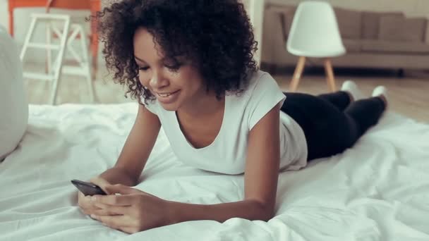 Όμορφο Αφρικανική κορίτσι ξαπλωμένο στο κρεβάτι και χρησιμοποιούν το κινητό τους — Αρχείο Βίντεο