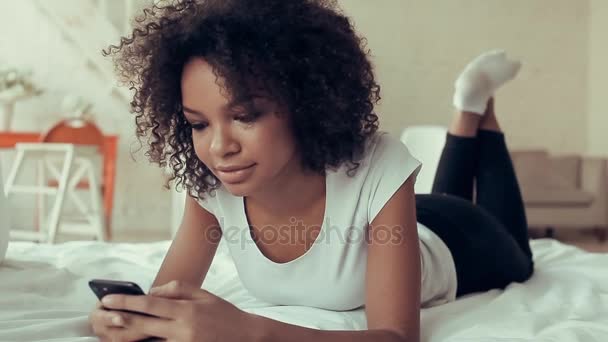 Mooie jonge Afrikaanse meisje liggen op het bed in de slaapkamer en de telefoon gebruiken — Stockvideo