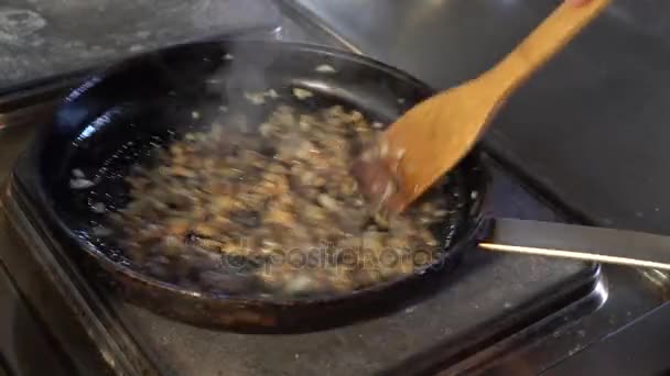 Cogumelos fritos com óleo em uma frigideira. Cozinheiro mexe cogumelos colher de madeira . — Vídeo de Stock