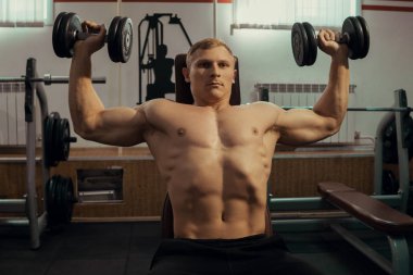 Yakışıklı adam kol kasları dumbbells ile spor salonunda sallanan