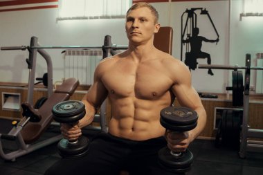 Yakışıklı adam kol kasları dumbbells ile bir spor salonunda sallanan