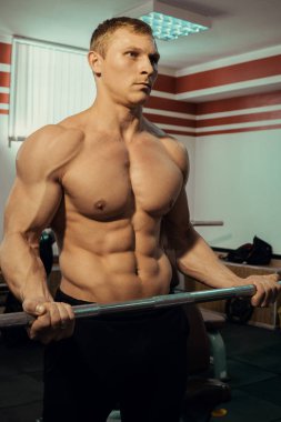 Genç kaslı adam çıplak gövde ile spor salonunda çıtayı yükseltiyor. Fitness