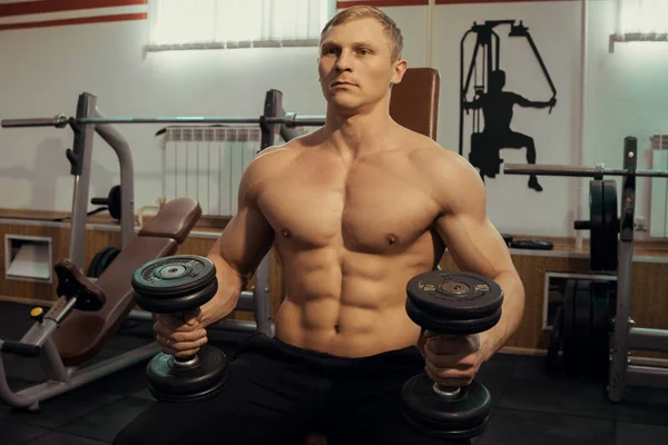 Handsome man swinging arm muscles with dumbbells in a gym
