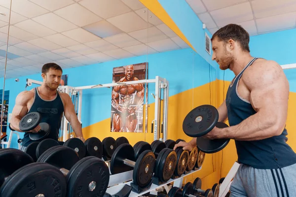 Un grand bodybuilder mâle fort faisant une presse de banc dans le miroir, fait un gros biceps en utilisant un haltère dans la salle de gym . — Photo