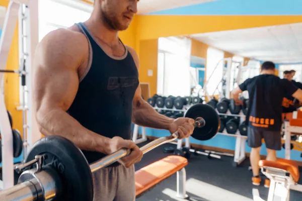 Un grand bodybuilder puissant et puissant soulève un haltère dans la salle de gym. Pompage d'un biceps puissant. Corps masculin sexy . — Photo