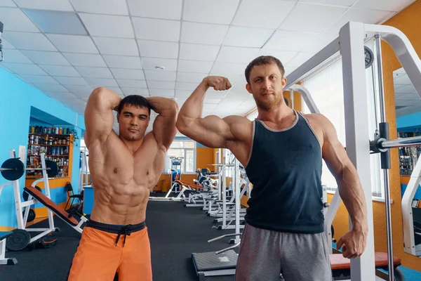 Mooie mannelijke bodybuilders met een naakte torso poseren in de sportschool. een sterke mannelijke figuur, krachtige lichaam, gepompt biceps, banken, pers. — Stockfoto