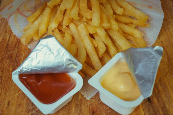 Patatine fritte tradizionali in un pacchetto con ketchup e senape su una tavola di legno — Foto Stock