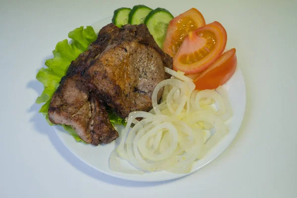 Carne a la parrilla jugosa en un plato blanco con cebollas, pepinos y tomates y una ensalada . — Foto de Stock