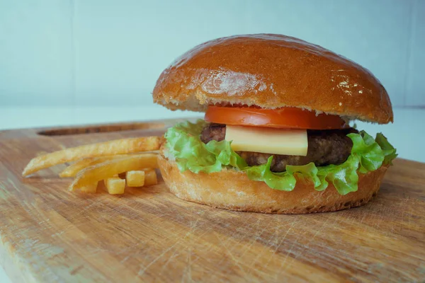 Um hambúrguer americano tradicional com costeleta, tomate e queijo em uma folha de salada. Batatas fritas. fast food . — Fotografia de Stock