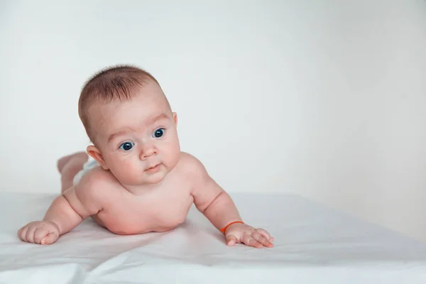 Un bebé divertido con hermosos ojos yace sobre su estómago y sonríe . —  Fotos de Stock