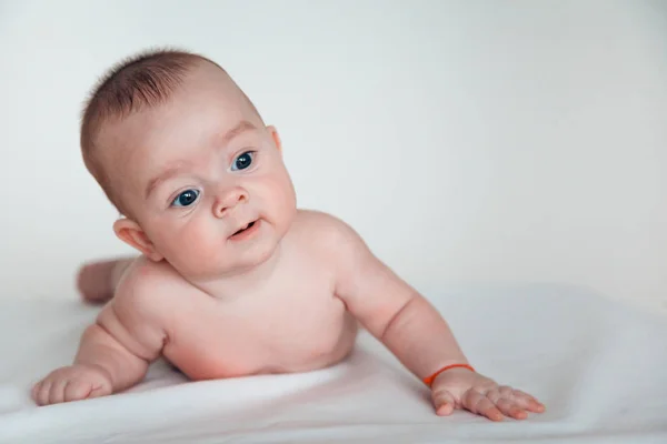 Un bebé divertido con hermosos ojos yace sobre su estómago y sonríe . —  Fotos de Stock