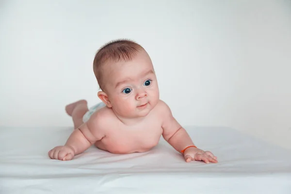 Un bebé divertido con hermosos ojos yace sobre su estómago y sonríe . —  Fotos de Stock