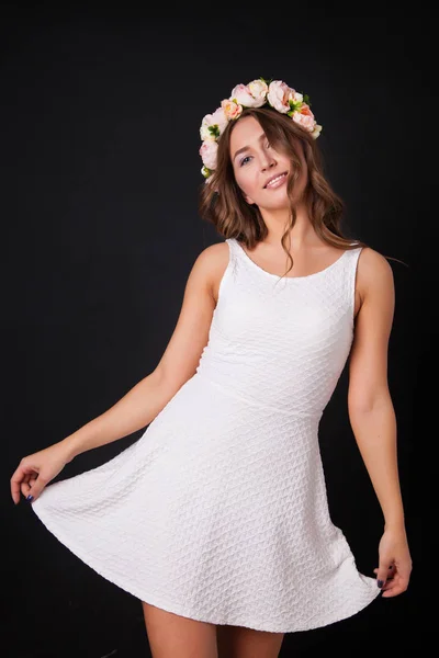 Hermosa chica en un vestido blanco con flores en la cabeza sobre un fondo negro —  Fotos de Stock