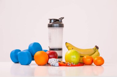 Sağlıklı bir diyet kavramı. Fintes yemek. Spor yaşam tarzı. Halter. Shaker. Portakal. Elma. Muz. meyve suyu. Atlama ipi. Ölçme bant bel. Beyaz bir arka plan üzerinde. Stüdyo çekim.